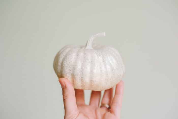Plastic gourd with gold glitter being held up by a hand in front of a blank wall.