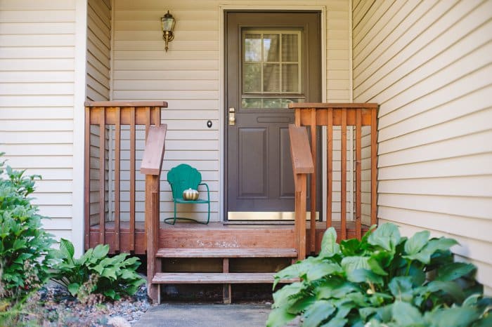 A painted white and gold plastic pumpkin sitting on a green chair on a front porch of a home.