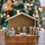 A handmade nativity set made with wooden peg dolls and clothing made of fabric scraps, pieces of ribbon, and bits of string, plus a handmade wooden stable.