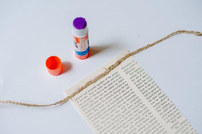 Using a glue stick to attach a piece of twine to the top of a paper flag.