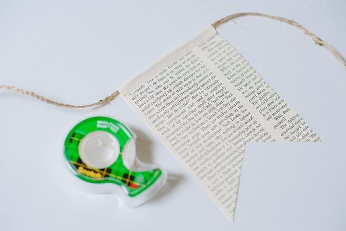 Securing a paper flag around twine using clear tape.