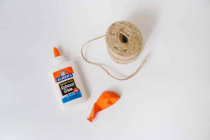 Elmers glue, a roll of twine, and a deflated balloon laying on a white background.