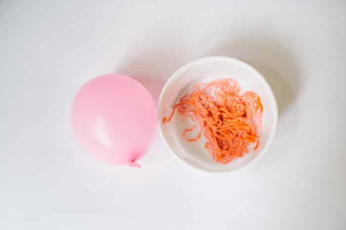 Orange yarn soaking in diluted glue in a bowl on a white background.