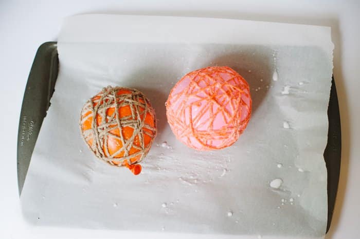 Two balloons wrapped with yarn and twine, drying on a cookie sheet lined with parchment paper.