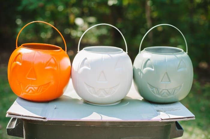 Three plastic Halloween treat buckets spray painted orange, white, and a green.