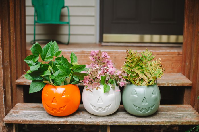 Three spray painted plastic Halloween treat buckets filled with plant clippings, sitting on a front porch.