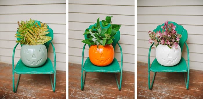 Three spray painted plastic pumpkin treat buckets filled with plant clippings on a small green metal chair on a front porch.