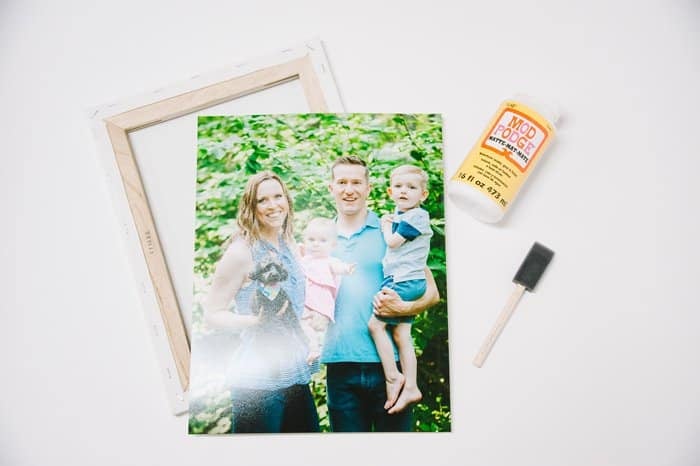 Supplies needed to make a diy canvas photo print. Canvas, photo, Mod Podge, and a foam brush laying on a white surface.