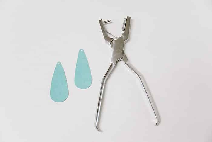 Punching a hole in the top of leather teardrop earrings with a leather punch.