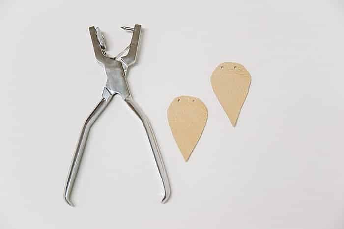 Punching two holes in the top of each leather leaf shape.