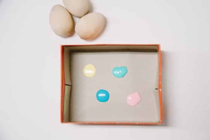 Wooden box with the lid removed, with four dots of pastel acrylic paint in side the box. Three wooden eggs sitting nearby.