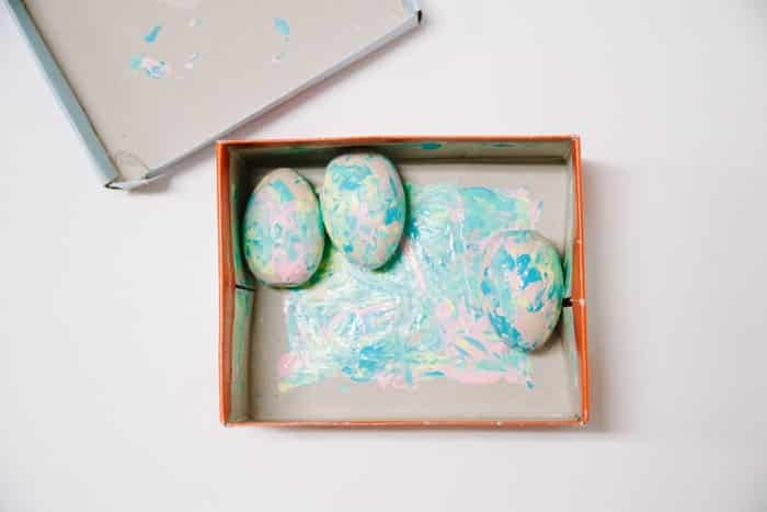 Wooden eggs with pastel paint swirled on them inside a cardboard box and lid.