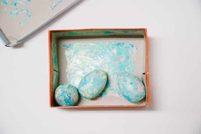 Wooden eggs with pastel paint swirled on them inside a cardboard box and lid.