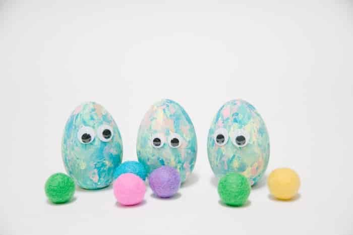 Pastel painted wooden eggs with googly eyes glued to them, surrounded by colorful felt balls.