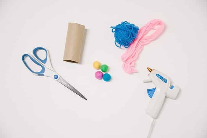 Supplies to make ice cream cones include a cardboard tube from inside toilet paper, yarn, scissors, and hot glue gun.