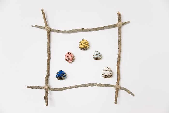 hang yarn wrapped pine cones from a picture frame made from sticks to make wall art