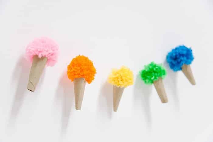 Ice cream cones made with cardboard cones and yarn pom tops in rainbow colors.