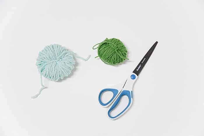Scissors and two yarn pom poms in the process of being made.