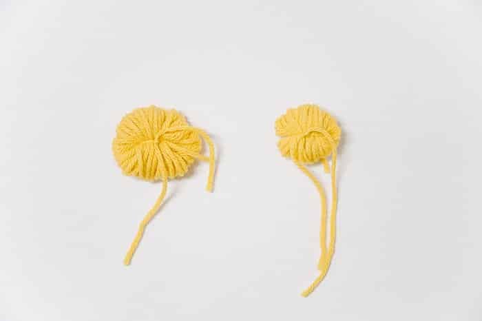 Two yellow half-finished yarn pom poms.
