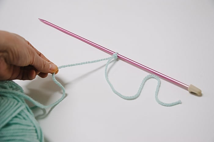 pull the long yarn tail to move the slip knot closer to your knitting needle