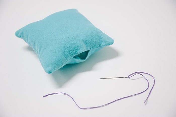 A pillow with a hole in it, and a needle and thread laying nearby.