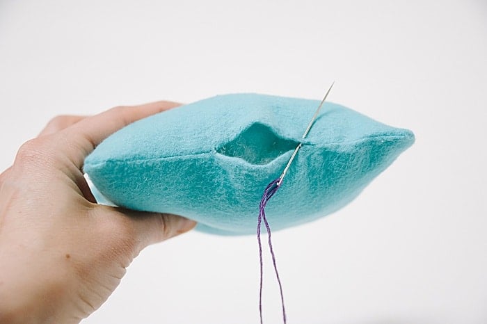A pillow with a hole in it, and a needle and thread starting to sew it closed.