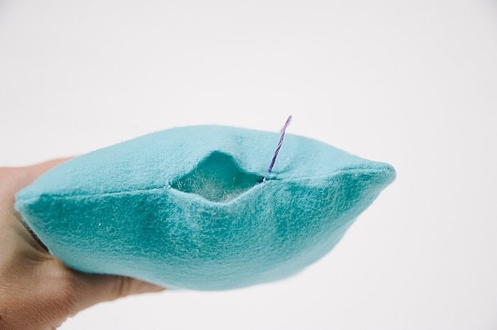 A pillow with a hole in it, and a needle and thread starting to sew it closed.
