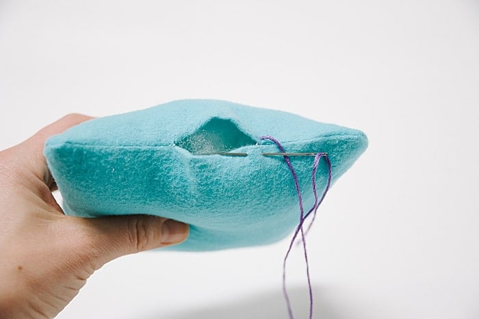 A pillow with a hole in it, and a needle and thread starting to sew it closed.