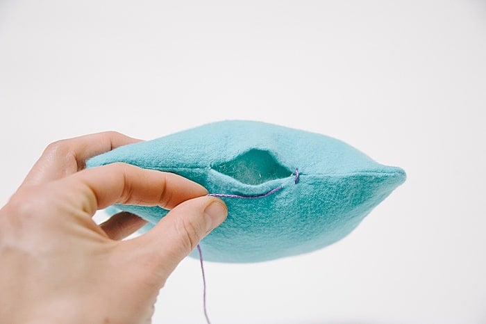 A pillow with a hole in it, and a needle and thread starting to sew it closed.