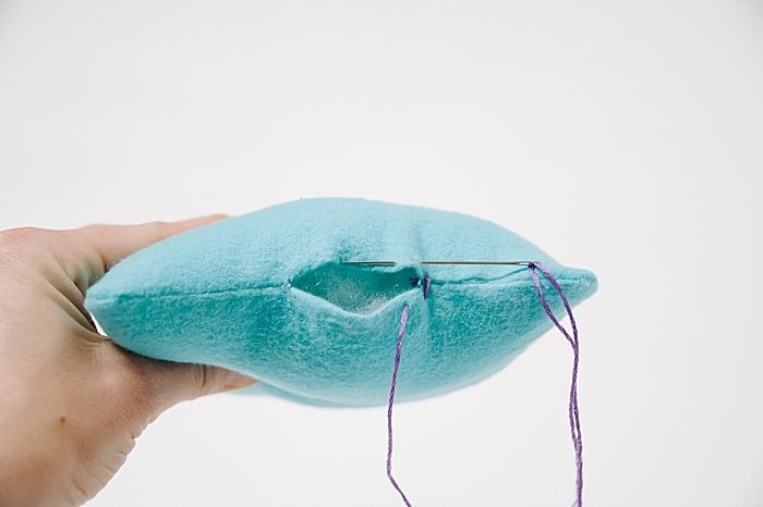 A pillow with a hole in it, and a needle and thread starting to sew it closed.