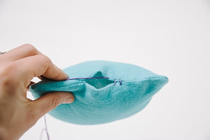 A pillow with a hole in it, and a needle and thread starting to sew it closed.