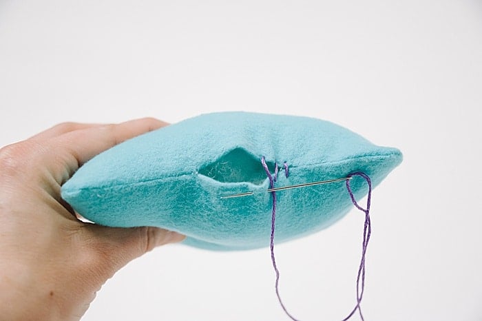 A pillow with a hole in it, and a needle and thread starting to sew it closed.
