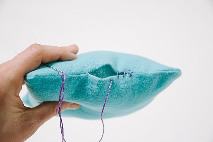 A pillow with a hole in it, and a needle and thread starting to sew it closed.