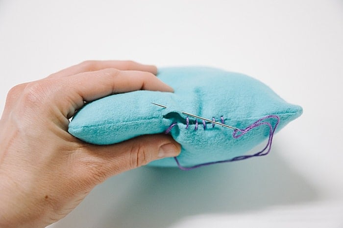 A pillow with a hole in it, and a needle and thread starting to sew it closed.