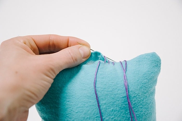 A pillow with a hole in it, and a needle and thread starting to sew it closed.