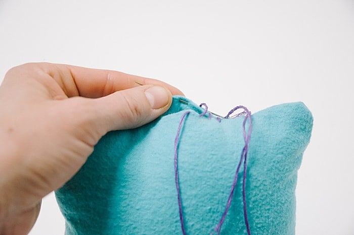 A pillow with a hole in it, and a needle and thread starting to sew it closed.