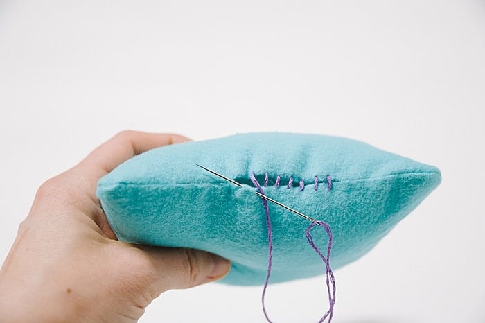 A pillow with a hole in it, and a needle and thread starting to sew it closed.