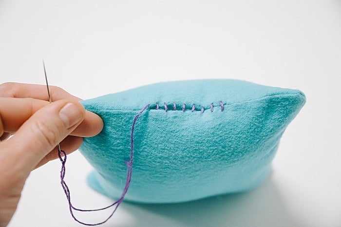 A pillow with a hole in it, and a needle and thread starting to sew it closed.