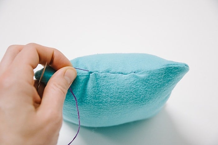A pillow with a hole in it, and a needle and thread starting to sew it closed.