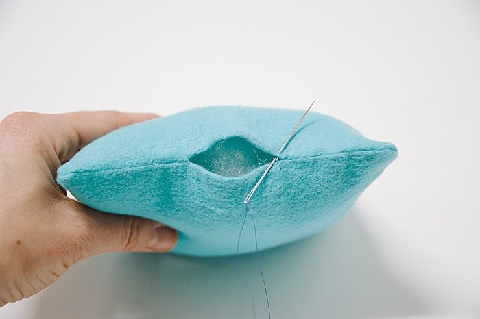 A pillow with a hole in it, and a needle and thread starting to sew it closed.