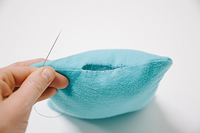 A pillow with a hole in it, and a needle and thread starting to sew it closed.