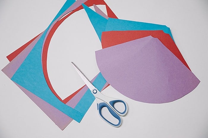 Red, purple, and blue paper cut into a cone template shape with scissors.