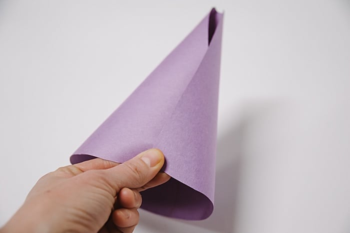 A purple piece of paper being rolled into a cone shape, and held in place by a hand.