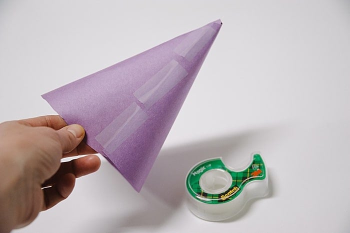 A purple paper cone with the seam taped with Scotch tape, and a roll of Scotch tape on the tabletop nearby.