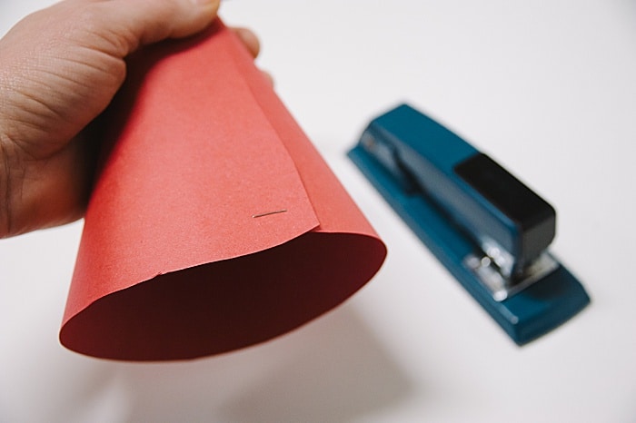 A red paper cone with a staple holding it together along the same, with a stapler on the tabletop nearby.