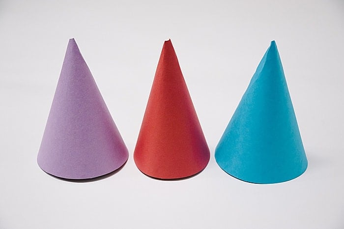 Three paper cones standing upright on a table. One is purple, one is red, and one is blue.