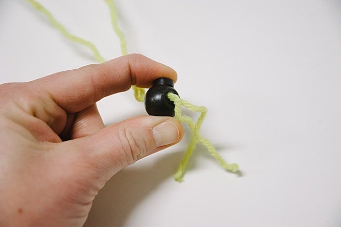 Fingers squeezing a black cord lock stopper with yellow yarn coming through it.