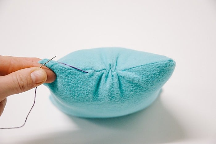 A pillow with a hole in it, and a needle and thread starting to sew it closed.