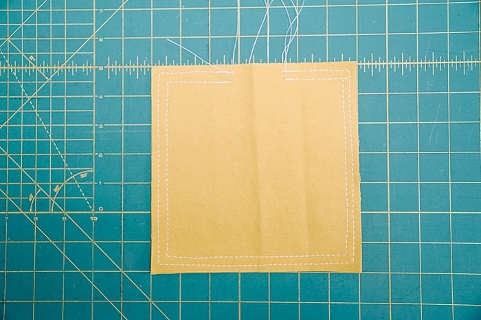 Two yellow squares of duck cloth fabric stacked and sewed twice around the perimeter, once with a ½ inch seam allowance and once with a ¼ inch seam allowance.