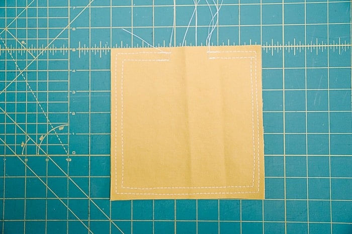 Two yellow squares of duck cloth fabric stacked and sewed twice around the perimeter, once with a ½ inch seam allowance and once with a ¼ inch seam allowance.